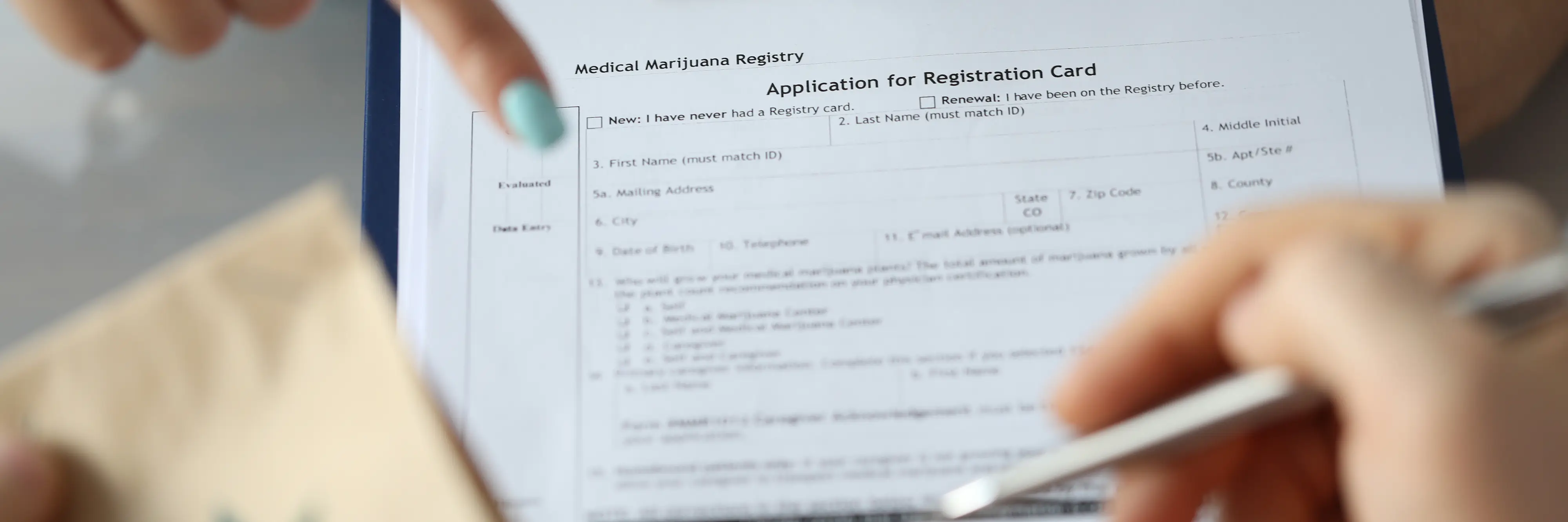 Close-up of a person filling out a Medical Marijuana Registry application form on a clipboard, with one hand holding a pen and the other pointing at the document.